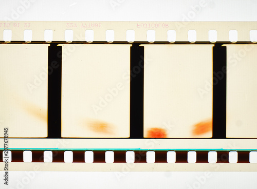 Vintage 35mm motion picture film strip featuring blank frames and classic sprocket holes. Authentic analog cinema celluloid isolated on white with orange light leak burn marks