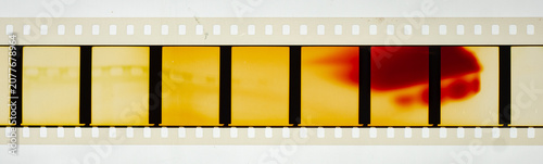 Long horizontal vintage 35mm motion picture film strip featuring blank frames and classic sprocket holes. Authentic analog cinema celluloid isolated on a white background with a red light leak burn