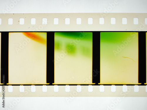 Vintage 35mm motion picture film strip featuring blank frames and classic sprocket holes. Authentic analog cinema celluloid isolated on white with green and orange light leak color effects