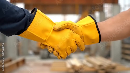 Two construction workers in yellow safety gloves shaking hands, symbolizing teamwork and successful completion of a project on a construction site