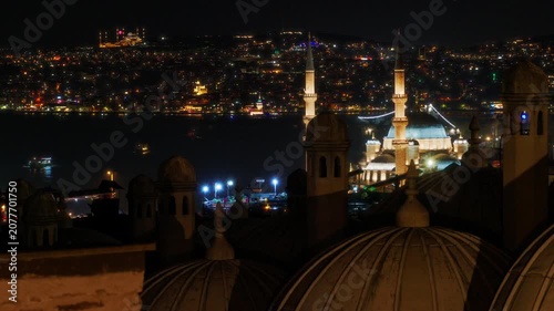 A breathtaking night view of the Istanbul skyline featuring an illuminated mosque with minarets overlooking the dark Bosphorus sea and glowing city lights across the hills