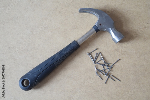 Steel claw hammer with a black rubber grip handle and metal nails on a wooden fiberboard background 