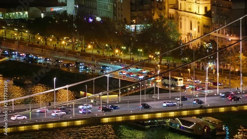 High angle view of the illuminated Erzsebet Bridge in Budapest at night with flowing car traffic, river cruises on the Danube, and glowing city lights under a dark sky
