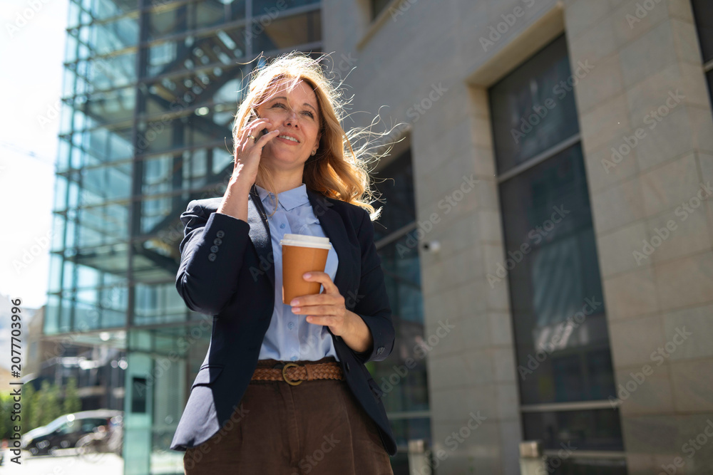 Fototapeta premium Businesswoman talking on phone with coffee in city