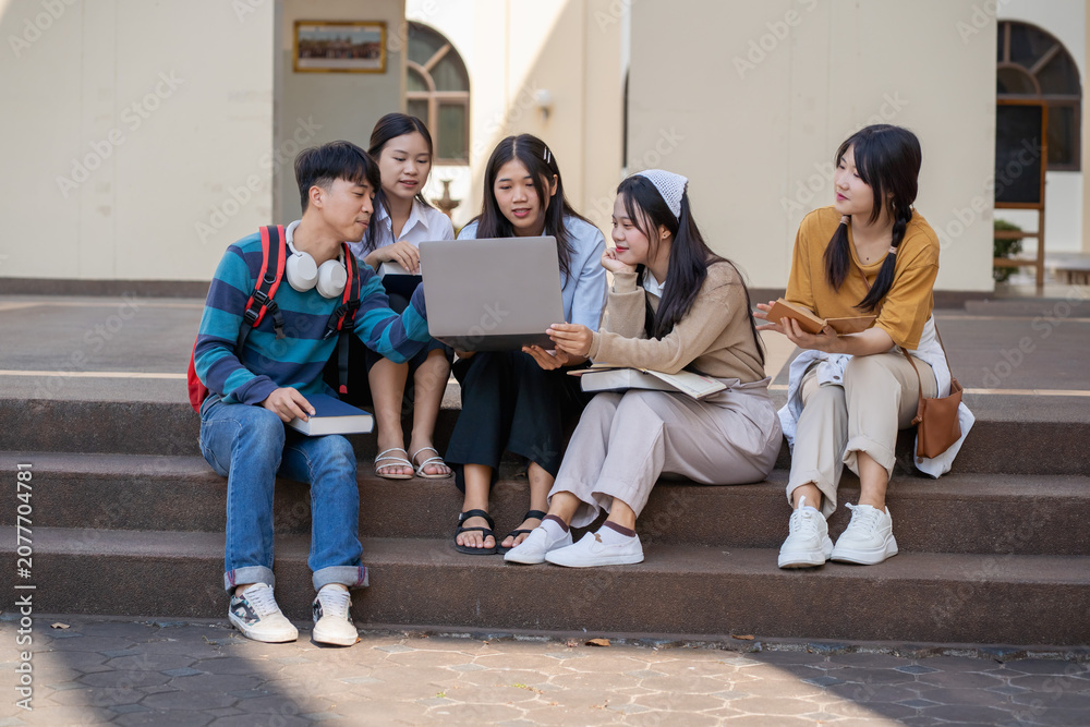 Fototapeta premium Diverse group of students working together on a laptop outside on a university campus