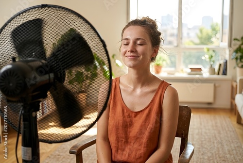 Young woman cooling down in front of an electric fan at home