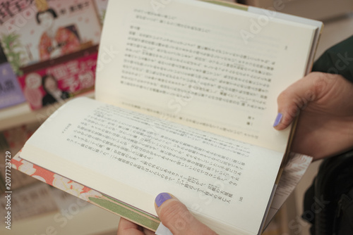 Fotografie Person holding open Japanese book with visible text, browsing pages in a booksto
