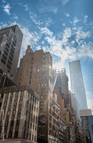New york, usa august 19,2024. New york city skyscrapers rise over manhattan streets under a partly cloudy blue sky, sunlight streaming across glass and concrete