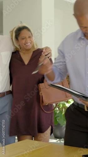 Vertical video: Handing keys man in light-blue shirt finishing portfolio at home as couple enters