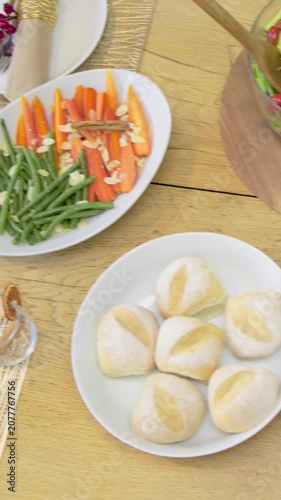 Vertical video: Drifting camera revealing home table meal spread with salad showcasing bread rolls