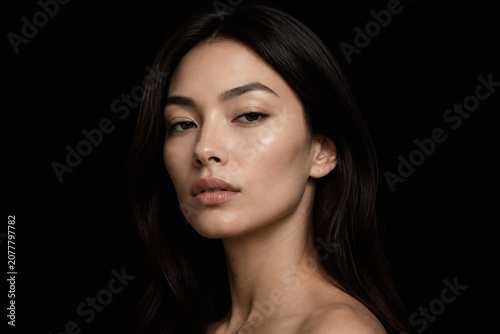 A young woman with long dark hair is posing against a black background.