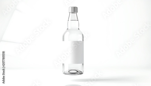 A clear glass bottle stands on a white surface with a silver cap and a blank white label in a minimalist interior.