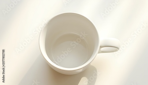 A white coffee mug sits empty on a plain surface with sunlight casting shadows.