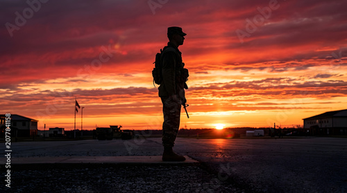 Soldier stands guard at sunset over military base with rifle in hand