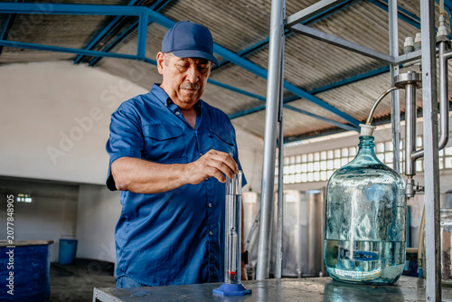 Obraz na plátně Distillery worker testing alcohol levels with a glass hydrometer tube