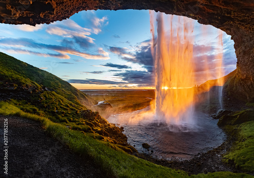 Quadro su tela Impressive waterfall “Seljalandsfoss“ in Iceland seen from a cave behind the sunlit water curtain at midnight in June