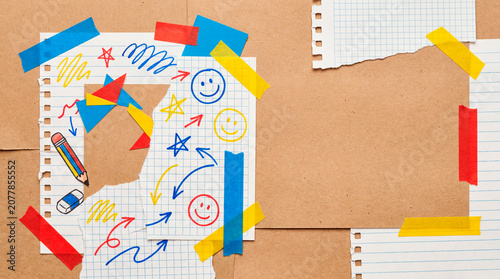 Childlike doodles on torn paper taped over cardboard with colorful school sketches