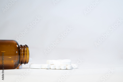 White medicine pills spilling out of an amber glass bottle on white background, pharmaceutical research and healthcare concept with copy space.