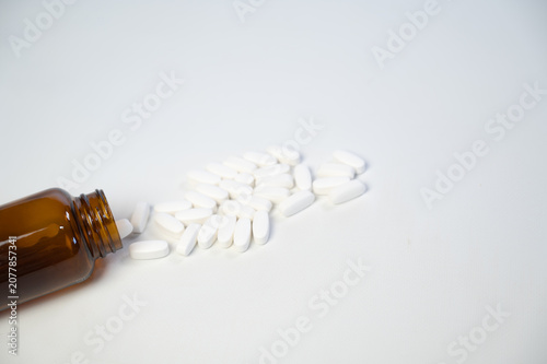 White medicine pills spilling out of an amber glass bottle on white background, pharmaceutical research and healthcare concept with copy space.