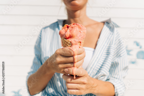 Woman holds a melting strawberry ice cream cone toward the camera.