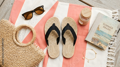 Pair of flip flops with sunglasses and straw bag on a beach towel for summer vacation