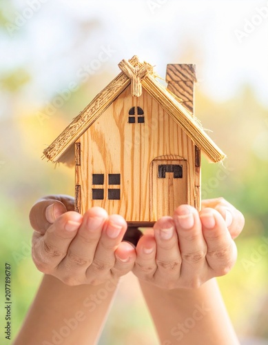 Hands holding a miniature model of a house against a blurred background