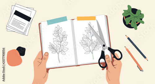 Top view of hands holding scissors to cut templates from an opened notebook on a creative workspace table.