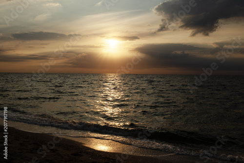 Peaceful sunrise over the calm sea with golden light on a sandy beach