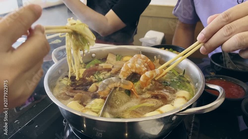 Close up of friends sharing traditional Asian hot pot. Hands using chopstick to pick up shrimp and meat from boiling soup.