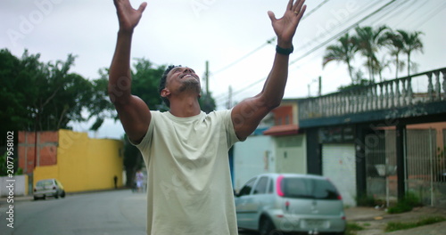 Foto Man of African descent standing on urban street with arms raised, looking up in