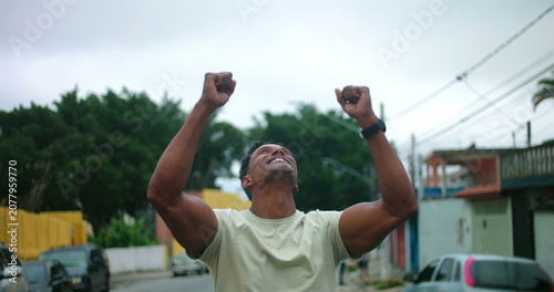 Fotografie Man of African descent standing on urban street with arms raised, looking up in