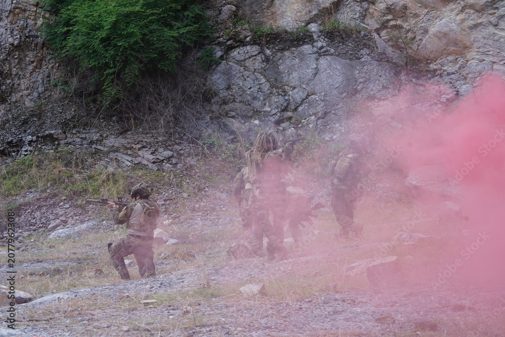 Fototapeta premium multinational group of male soldiers in infantry uniforms, carrying paintball guns and ready for combat, with pink smoke grenades and practicing military drills, with pink smoke signals