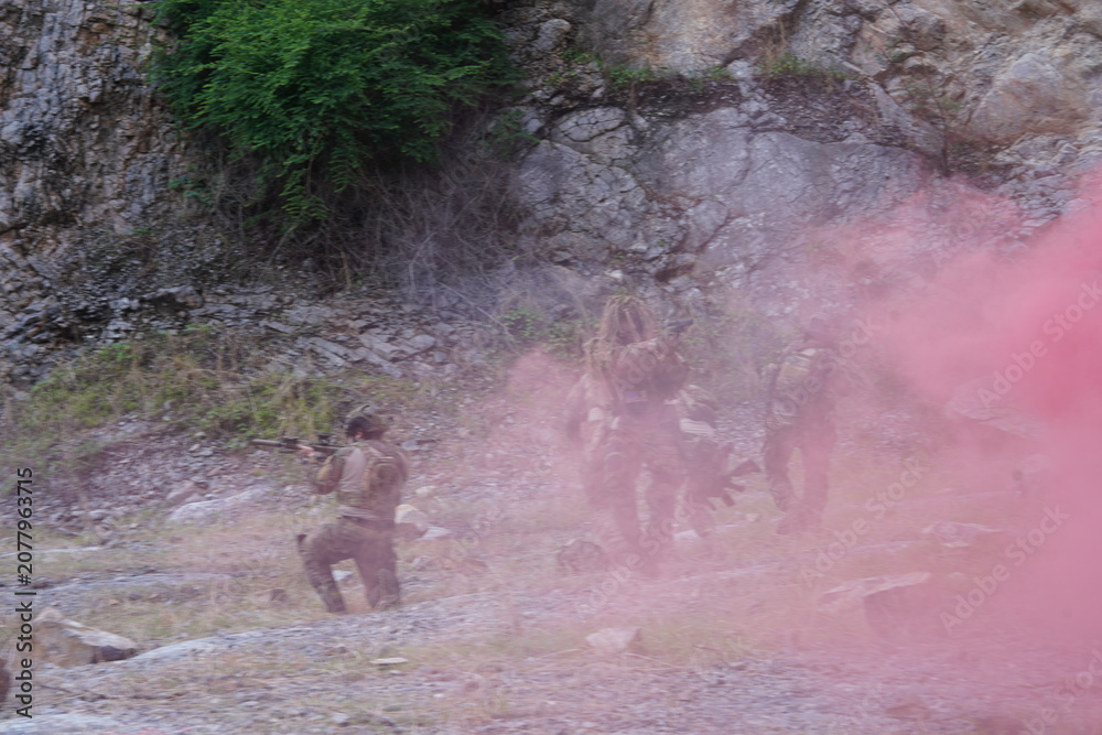 Fototapeta premium multinational group of male soldiers in infantry uniforms, carrying paintball guns and ready for combat, with pink smoke grenades and practicing military drills, with pink smoke signals
