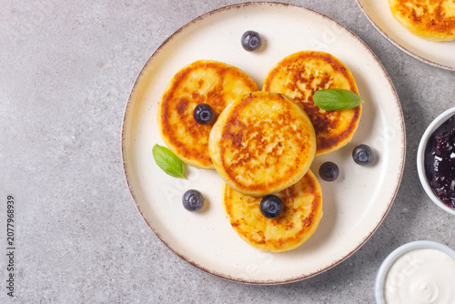 Golden cottage cheese pancakes with sour cream, blueberry jam and fresh berries. Healthy breakfast concept.