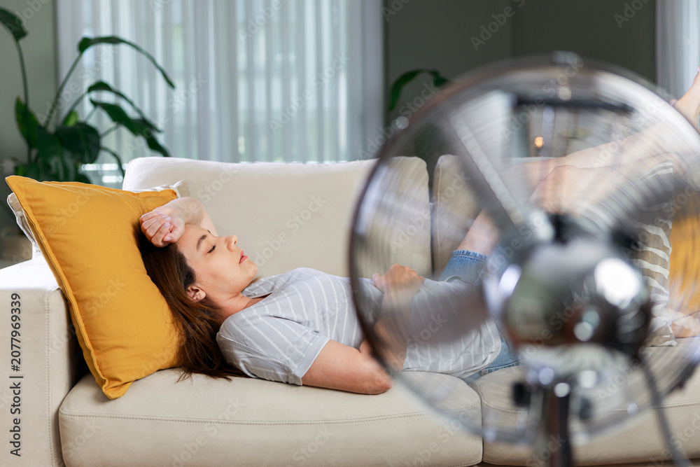 Fototapeta premium Woman resting in front of electric fan during heatwave