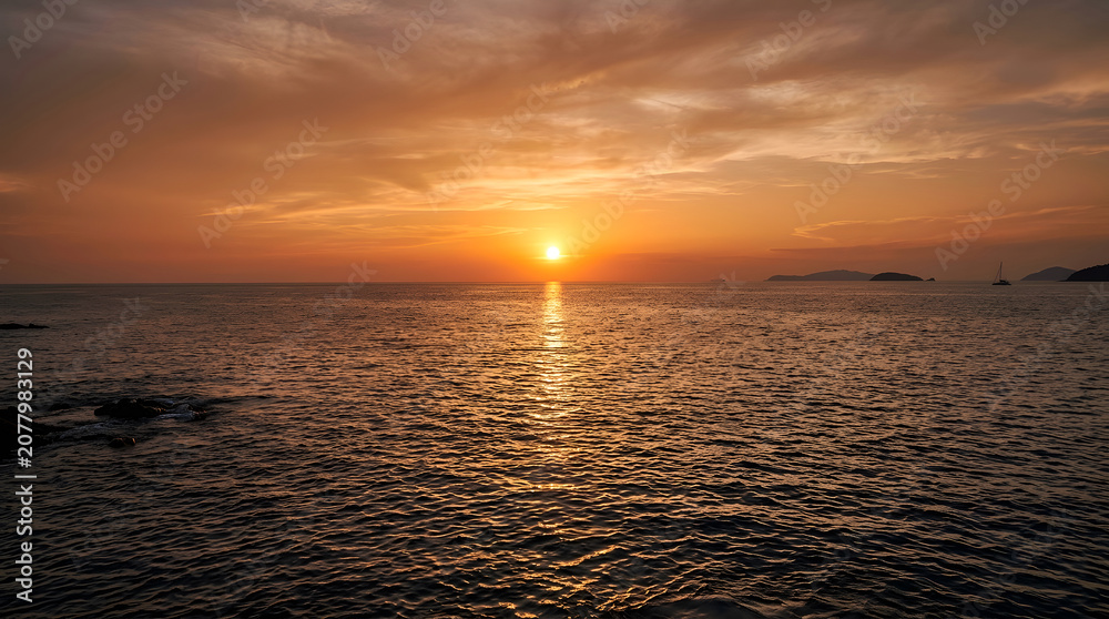 Obraz premium Sunset over calm ocean water with distant islands and warm orange sky