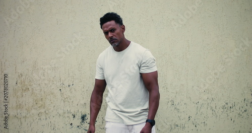 Schilderij op canvas Man of African descent standing against textured wall, pointing forward with ser