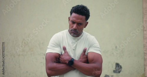 Obraz na plátně Man of African descent standing against textured wall with arms crossed, intense