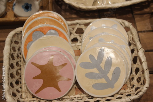 Round ceramic coasters with painted plant and organic leaf motifs in wicker basket.