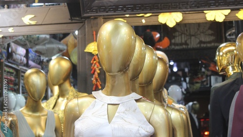 Group of golden mannequins in front of clothing shop showing stylish fashion items.