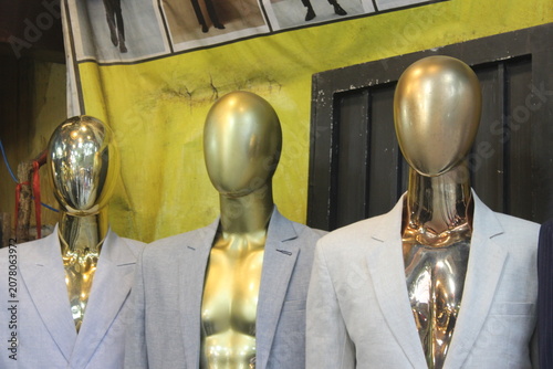 Three headless golden mannequins wearing formal blazers standing in clothing store.