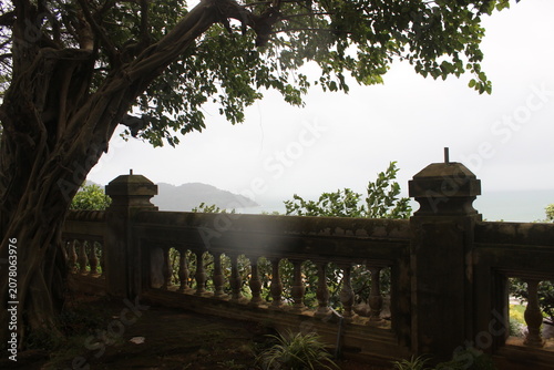Ornate stone balustrade railing framing view of distant mountains across calm sea.