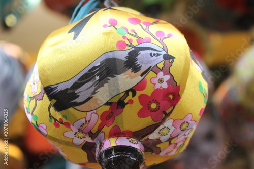 Decorative fabric lantern with bird illustration hanging in a traditional market.
