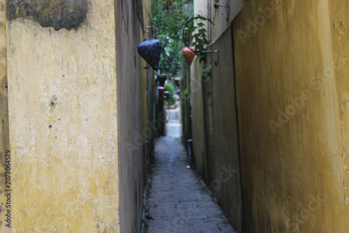 View through narrow urban alleyway with aged yellow walls and hanging light decor.