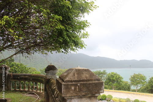 Concrete stone balustrade fence overlooking sea bay and mountain range in greenery.