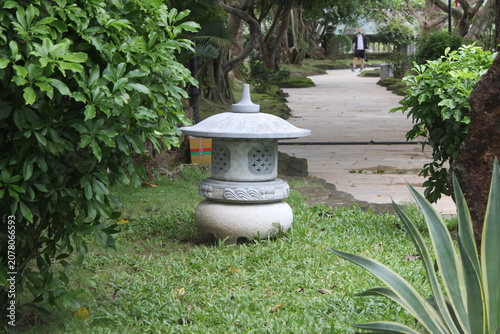 Traditional stone garden lantern standing on green grass near winding stone paths.