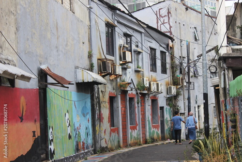 People walking through narrow alleyway decorated with creative street art wall paint.
