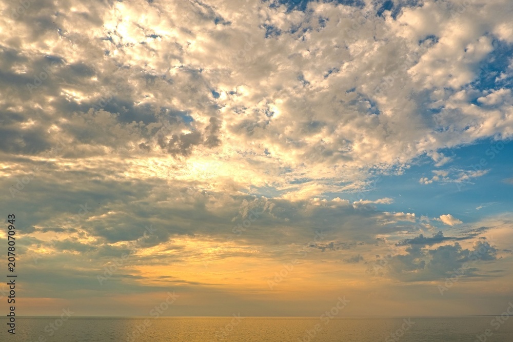 Fototapeta premium Scenic sunset sky filled with dramatic fluffy clouds over the calm sea horizon at golden hour.