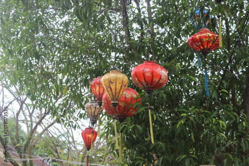 Collection of vibrant red and yellow patterned fabric lanterns hanging from trees.