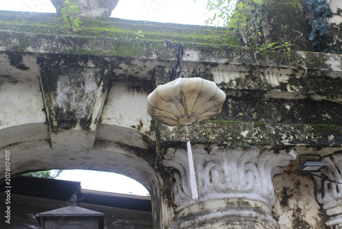 White fabric lantern suspended from weathered stone archway with mossy architecture.